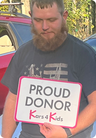 A person holding a sign that says Proud Donor Kars4Kids