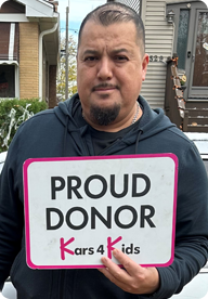 A person holding a sign that says Proud Donor Kars4Kids