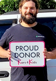 A person holding a sign that says Proud Donor Kars4Kids