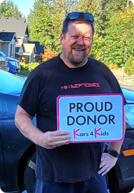 A person holding a sign that says Proud Donor Kars4Kids