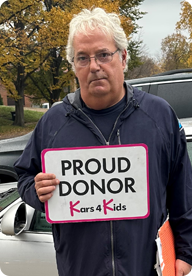 A person holding a sign that says Proud Donor Kars4Kids