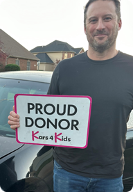 A person holding a sign that says Proud Donor Kars4Kids