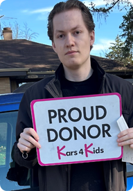 A person holding a sign that says Proud Donor Kars4Kids